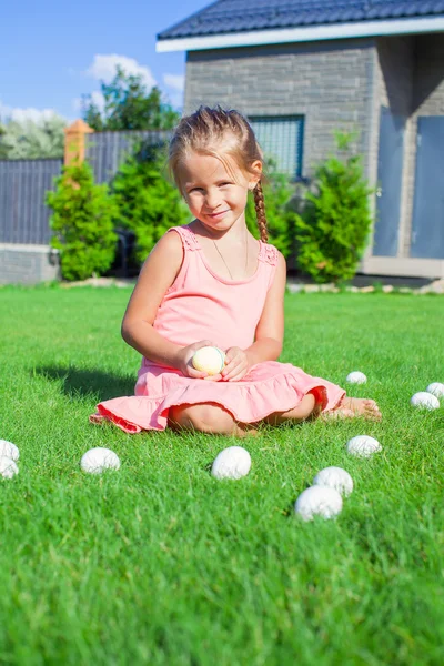 Piccola ragazza adorabile che gioca con uova di Pasqua bianche nel cortile — Foto Stock