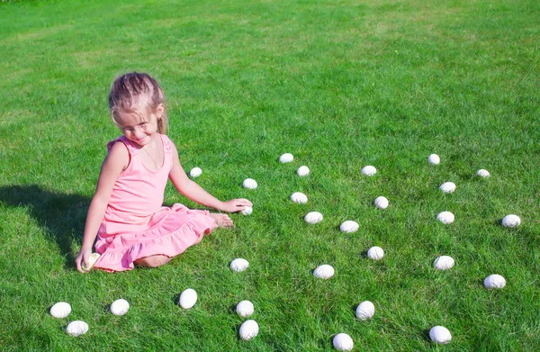 Маленькая девочка с белыми пасхальными яйцами во дворе на зеленой траве — стоковое фото