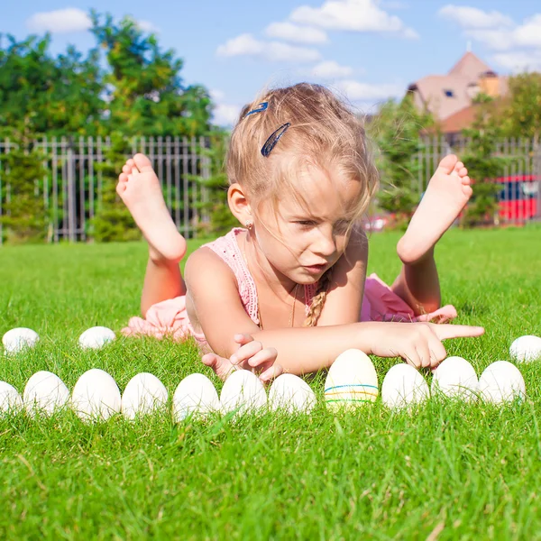 Kleines fröhliches und lustiges Mädchen spielt mit Ostereiern auf grünem Gras — Stockfoto