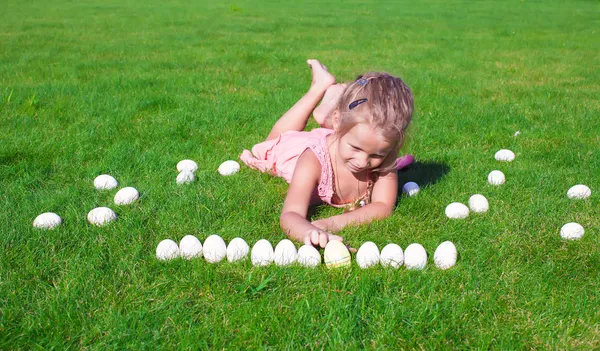 Маленькая очаровательная девочка играет с белыми пасхальными яйцами во дворе — стоковое фото