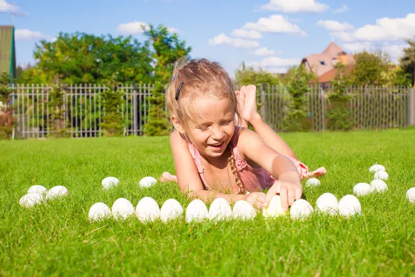 Kleines entzückendes Mädchen spielt mit weißen Ostereiern im Hof — Stockfoto