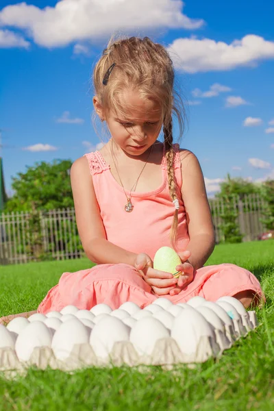Очаровательная маленькая девочка с зеленым пасхальным яйцом сидит снаружи — стоковое фото