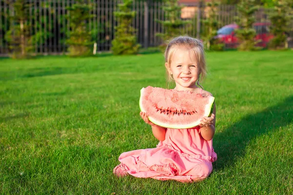 Little girl with big piece of watermelon in hands on green grass — Stock Photo, Image