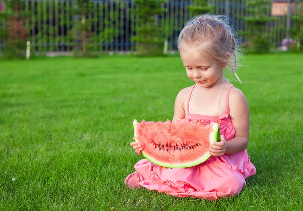 Little girl with big piece of watermelon in hands on green grass — Stock Photo, Image