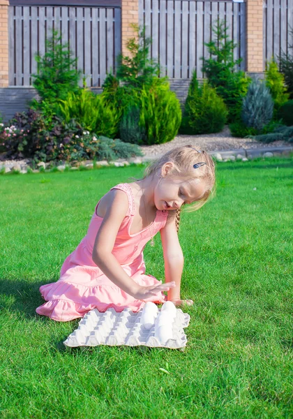 Kleines entzückendes Mädchen spielt mit weißen Ostereiern im Hof — Stockfoto