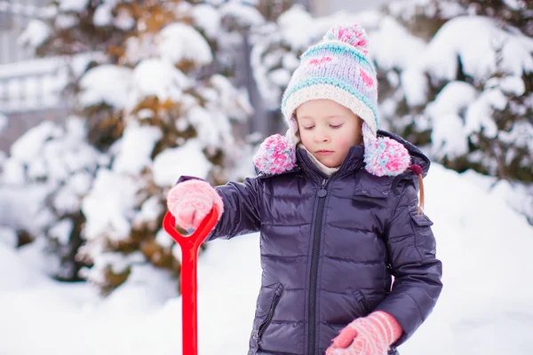 Little girl playing with red shovel in the garden on winter day — Stock Photo, Image