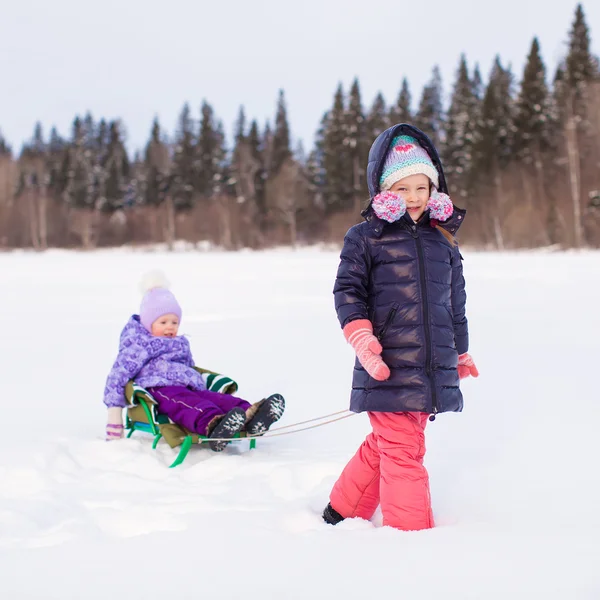 Adorable happy girl sledding her little sister — Stock Photo, Image