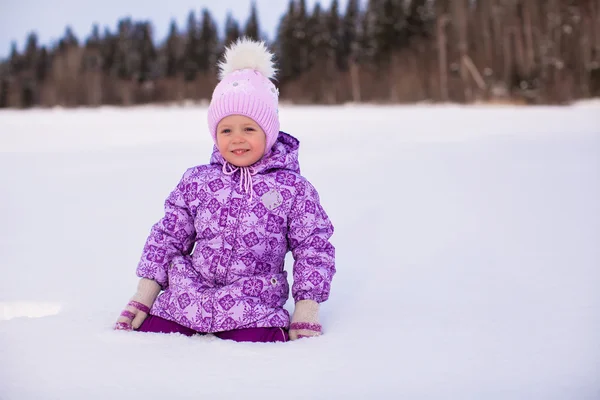 可爱的小姑娘坐在雪地上，在冬天阳光明媚的日子 — 图库照片