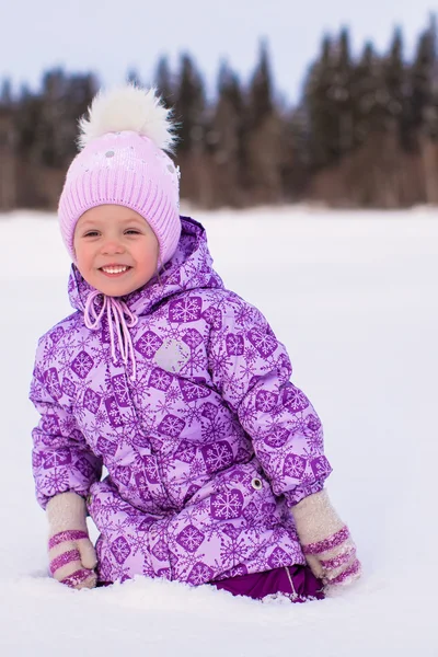 Little happy adorable girl sitting on the snow at winter sunny day — Stock Photo, Image