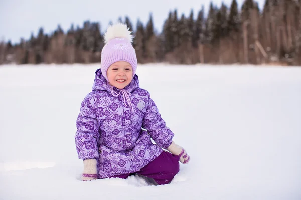 可爱的小姑娘坐在雪地上，在冬天阳光明媚的日子 — 图库照片