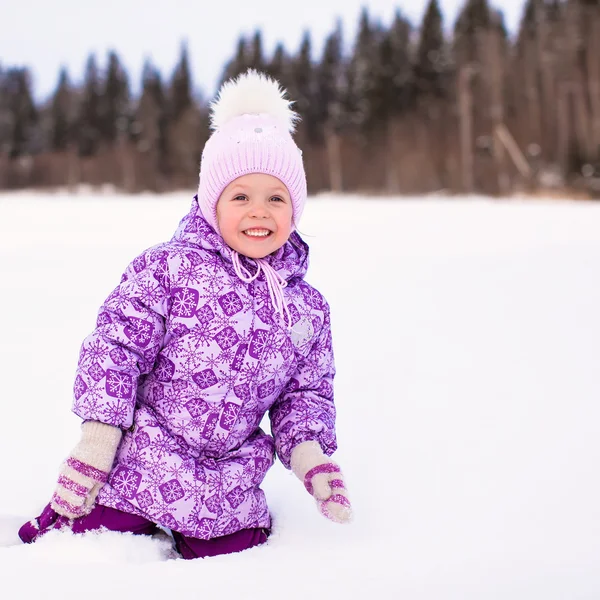 Pequena menina adorável feliz sentado na neve no inverno dia ensolarado — Fotografia de Stock