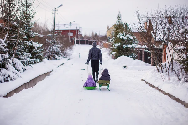 Junger Vater rollt seine kleinen süßen Töchter auf einem Schlitten in den Schnee — Stockfoto