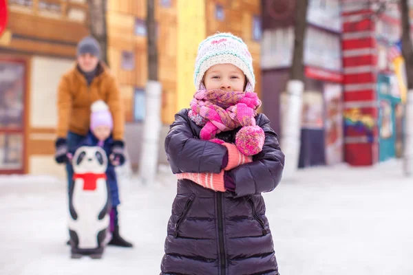 Charming girl on skating rink, dad with little sister in the background — Stock Photo, Image