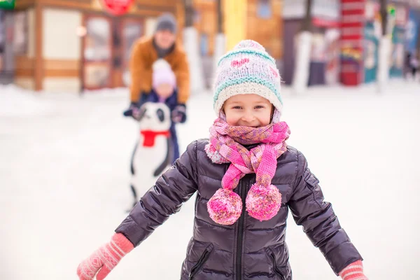 Adorable dziewczyna na lodowisko, tata z siostra w tle — Zdjęcie stockowe