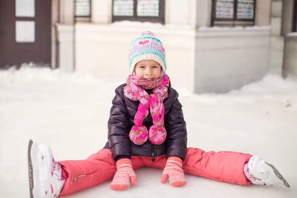 Маленькая очаровательная девочка, сидящая на льду с коньками после падения — стоковое фото