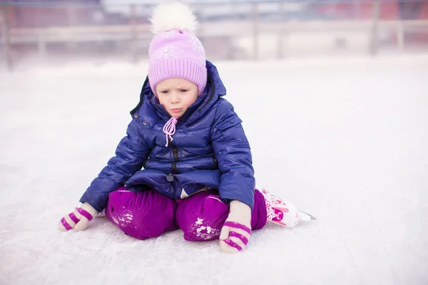 Adorable niña sentada en hielo con patines después de la caída —  Fotos de Stock