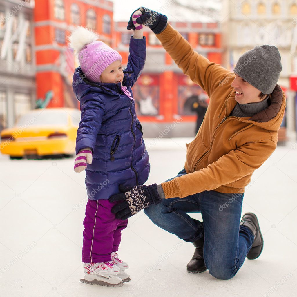 Young father and adorable little girl have fun on skating rink