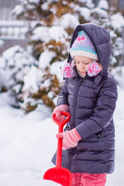 Malá dívka si hraje s červenou lopatkou v zahradě — Stock fotografie