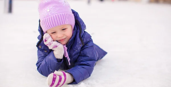 Entzückendes kleines Mädchen liegt nach dem Sturz auf der Eisbahn — Stockfoto