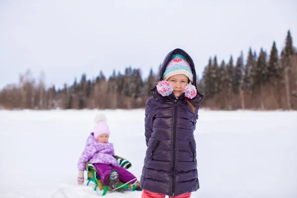 Adorable little happy girl sledding her sister — Stock Photo, Image