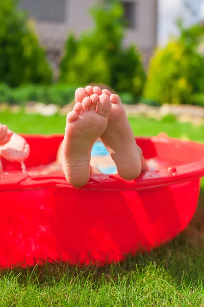 Primo piano delle gambe del bambino in una piccola piscina rossa — Foto Stock