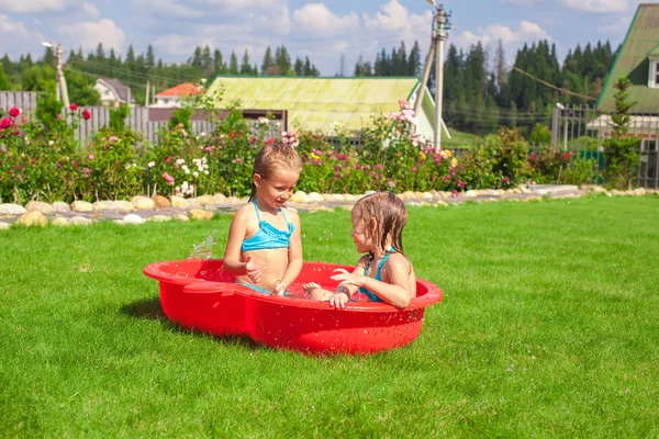 Two little sisters playing and splashing in the pool on a hot sunny day — Stock Photo, Image