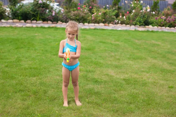 Niña adorable jugando con pistola de agua al aire libre en el soleado día de verano —  Fotos de Stock