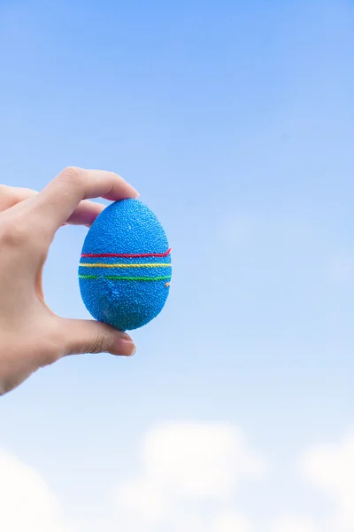 Brillante hermoso huevo de Pascua en la mano en el fondo del cielo azul —  Fotos de Stock