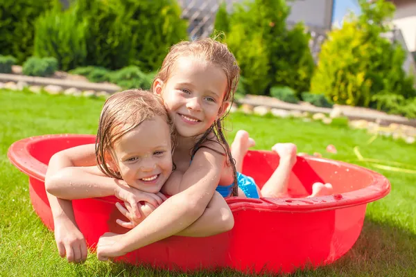 Dos hermanas pequeñas jugando y chapoteando en la piscina en un día soleado caliente — Foto de Stock