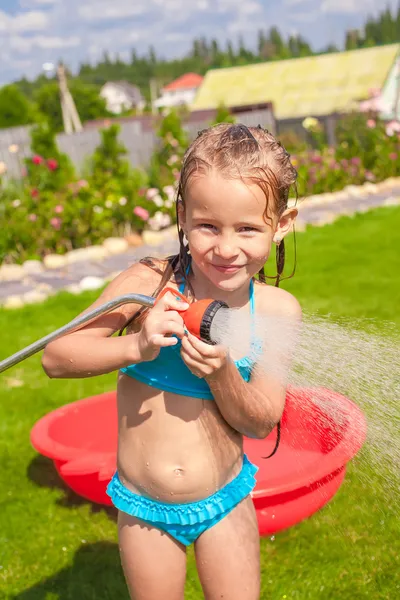 Menina adorável feliz sorrindo e derramando água de uma mangueira — Fotografia de Stock