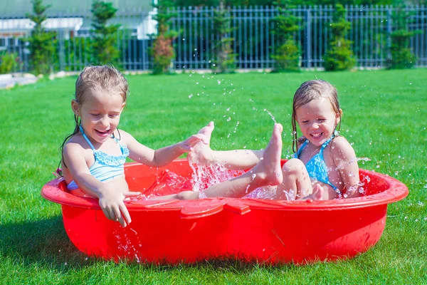Duas irmãs brincando e salpicando na piscina em um dia ensolarado quente — Fotografia de Stock