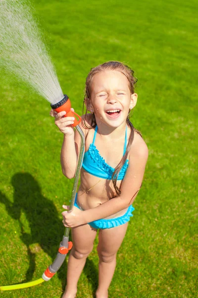 Šťastný roztomilá holčička vylévání vody z hadice a směje se — Stock fotografie