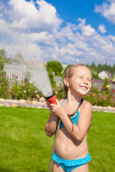 Feliz linda niña vertiendo agua de una manguera y riendo — Foto de Stock