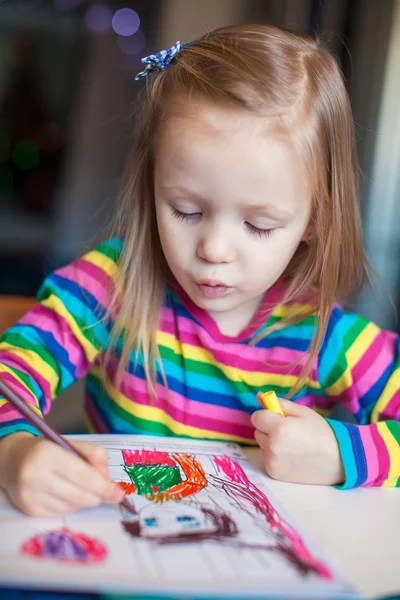 Маленькая милая девочка рисует карандашами, сидя за столом — стоковое фото