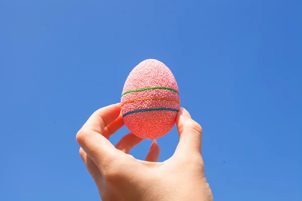 Brillante hermoso huevo de Pascua en la mano en el fondo del cielo azul — Foto de Stock