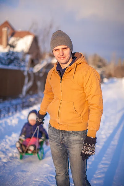 Jeune père traînant sa petite fille sur un traîneau dans la neige à l'extérieur — Photo