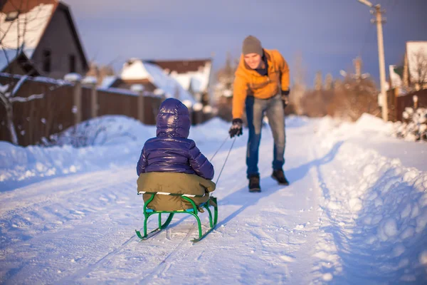 Young father sledding his little daughter on a sled in the snow outdoors — Stock Photo, Image