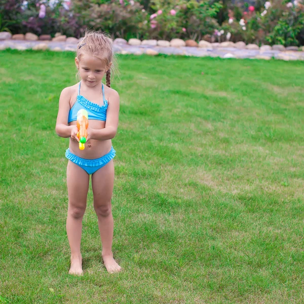 Little adorable girl playing with water gun outdoor in sunny summer day — Stock Photo, Image