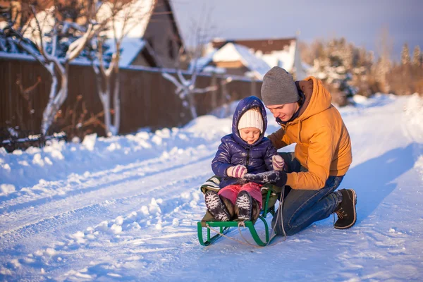 Junger Vater rodelt seine kleine entzückende Tochter an einem sonnigen Wintertag — Stockfoto