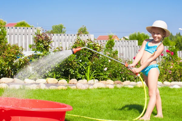 Rozkošná holčička vylévání vody z hadice a směje se — Stock fotografie