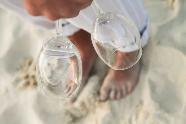 Closeup of two glasses in hand at man walking barefoot on the beach — Stock Photo, Image