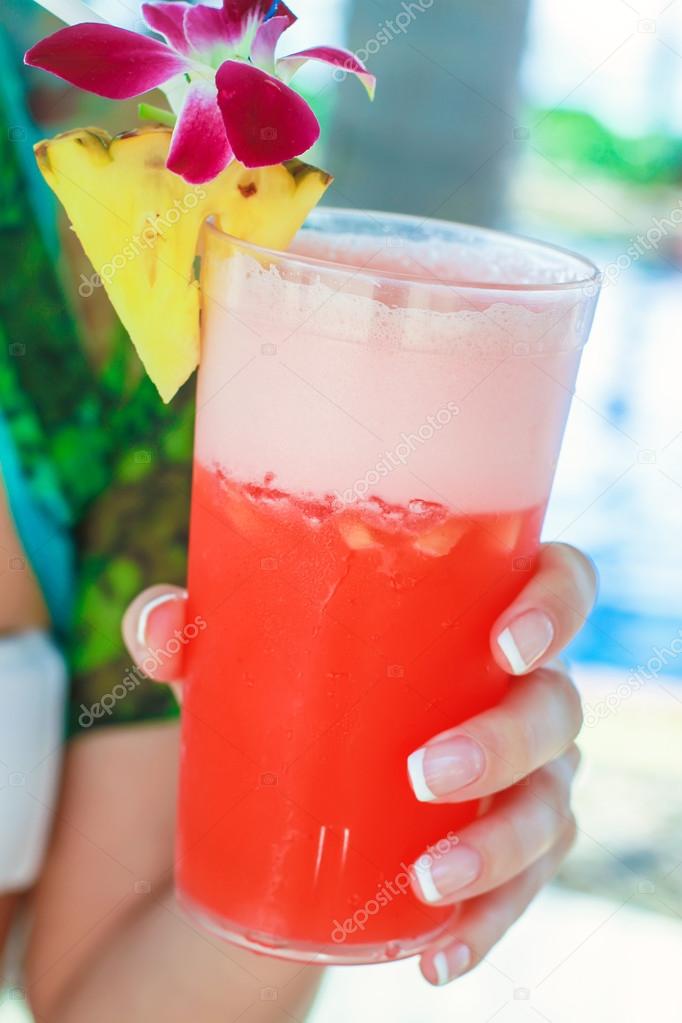 Tropical red cocktail in hand of a young woman on an exotic resort