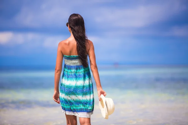 Vista trasera de la joven con sombrero en la mano en la playa exótica blanca mirando al mar — Foto de Stock