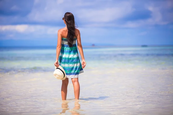 Vista trasera de la joven con sombrero en la mano en la playa exótica blanca mirando al mar —  Fotos de Stock