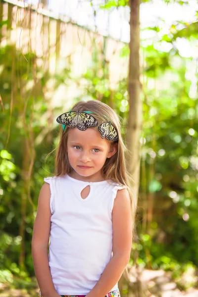 Liten bedårande flicka spelar med fjäril i fjärilar trädgård — Stockfoto