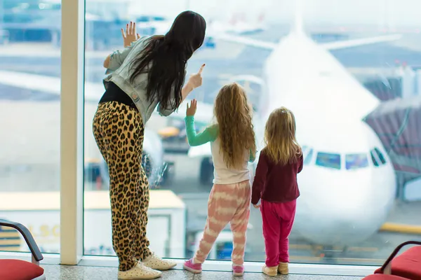 Маленькие милые девочки с мамой рядом с большим окном в аэропорту глядя на большой самолет — стоковое фото