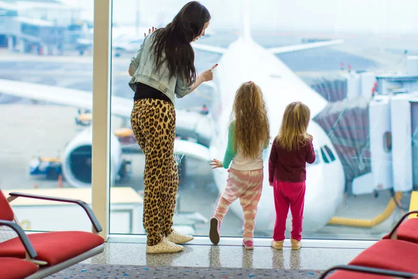 Little cute girls and young mother near large window in airport looking at the plane — Stock Photo, Image