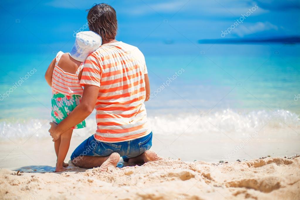 Father with little daughter relaxing on white beach