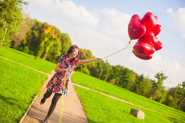 Šťastná dívka se bavit s červenými balóny mimo — Stock fotografie