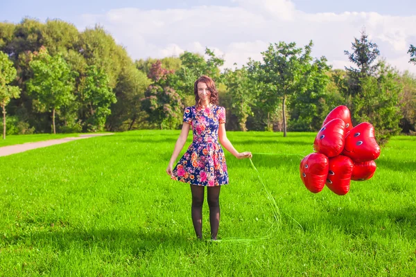 Ung glad kvinna med röda ballonger promenader i parken — Stockfoto